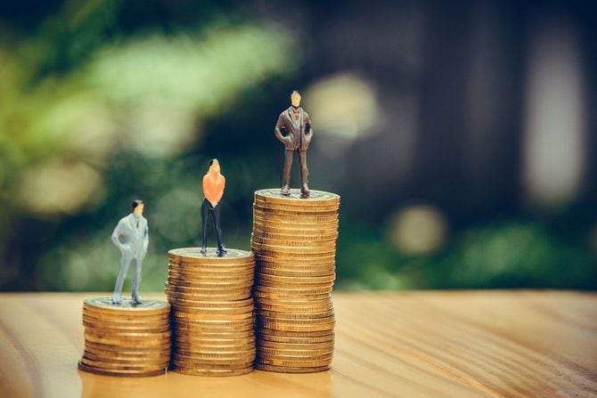 積み上げたコインの上に立っているミニチュアの人