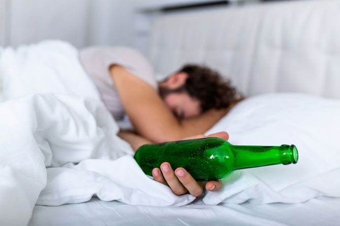 お酒の瓶を手に持ち、ベッドで眠る男性