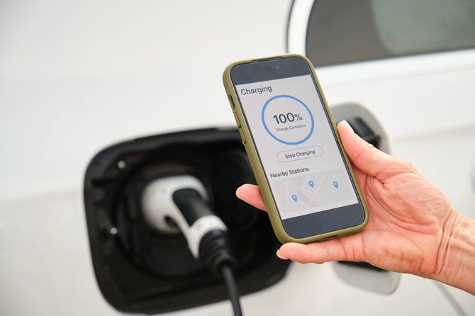 電気自動車の充電ステーションで100%充電が完了しているスマートフォンを持っている女性
