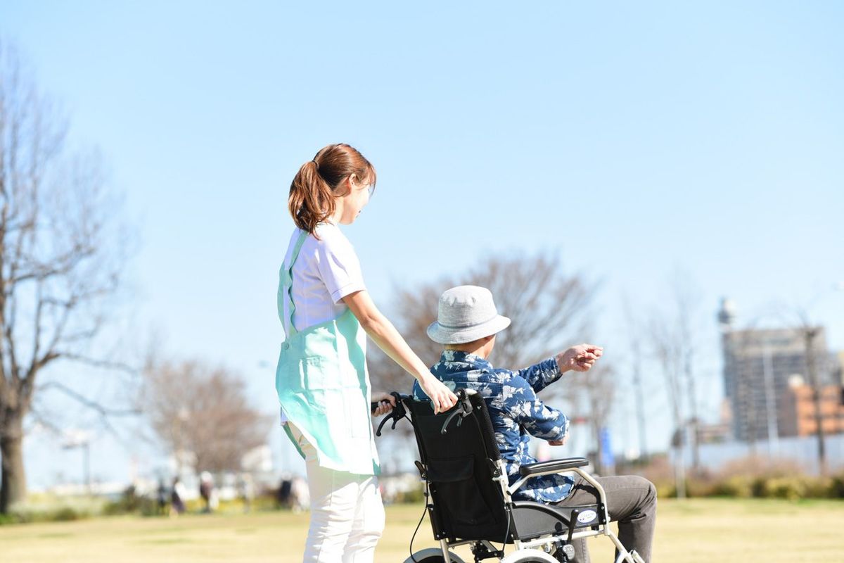車椅子に乗った高齢男性と歩く女性介護士
