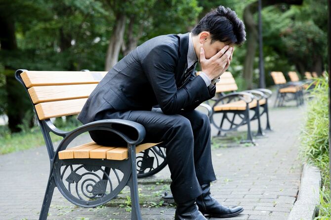 公園でうなだれる若いビジネスマン