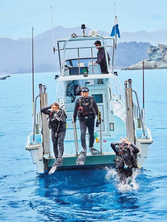 青空の中、小型船からダイビングスーツを着て海に入っていく野島さんたち。
