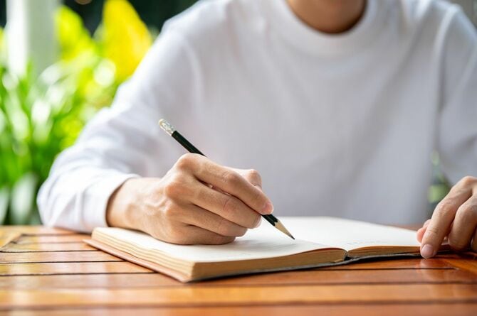 ノートに鉛筆で書いている男性の手