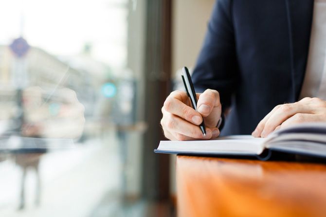 Businessman Writing in Planner at Cafe Window