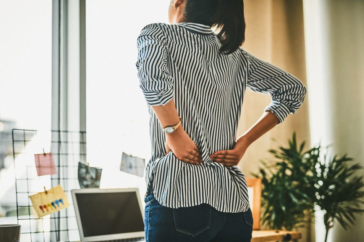 自宅で仕事中に背中の痛みに苦しむ若い女性