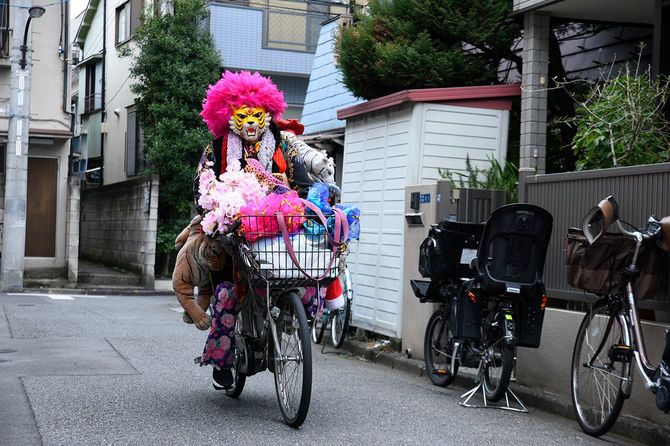 ピンクアフロのカツラにタイガーのお面をつけて自転車に乗る人