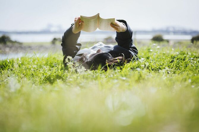 草の上に寝転んで本を読む人