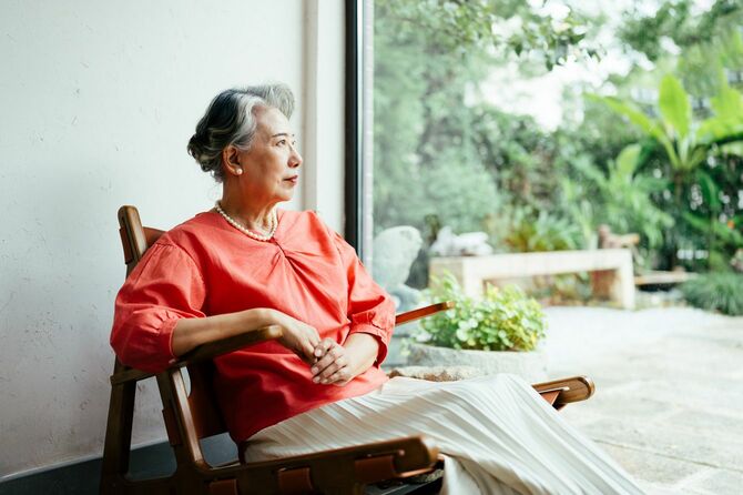 窓際の椅子に座りながら外を眺める年配の女性