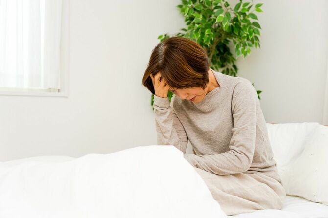 ベッドの上で頭の痛みを覚える女性