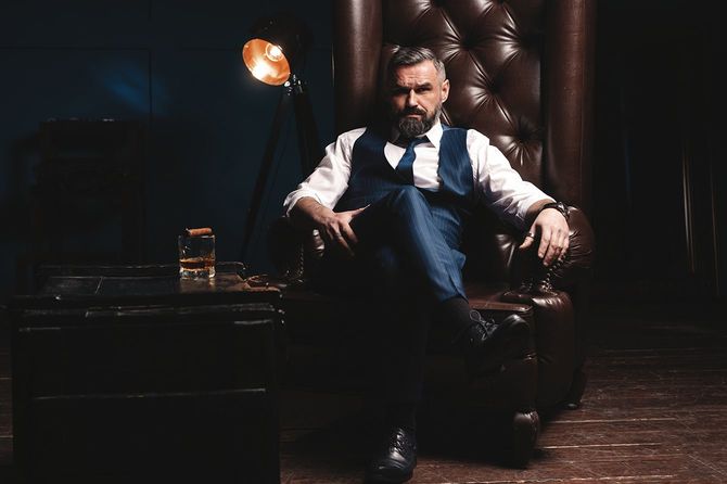 暗い部屋で葉巻とガラスのウイスキーを持つハンサムなエレガントな成熟した男の肖像画