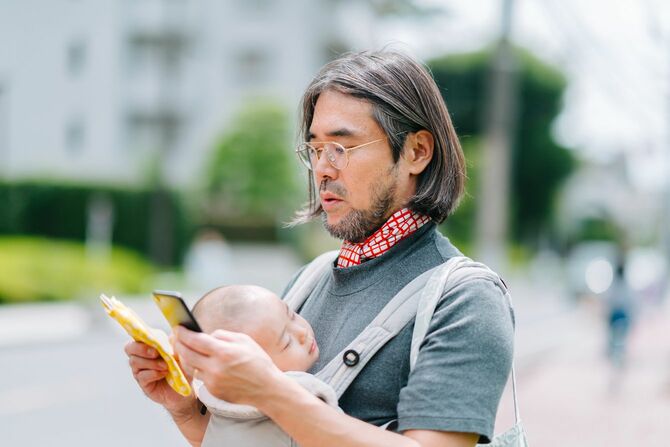 赤ちゃんを抱っこしながらスマートフォンをチェックする男性