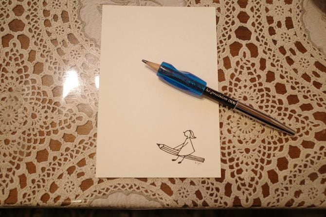 春日さんが愛用するグリップをはめた鉛筆。お孫さんのイラストが入ったはがきとともに