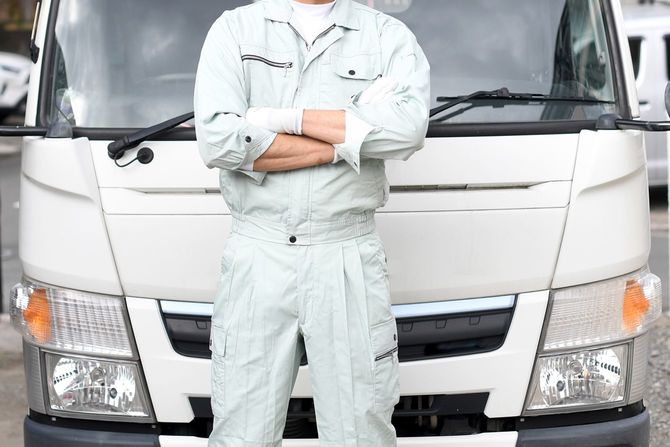 トラックの前で腕を組んで作業着を着た中年男性