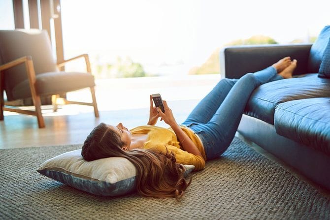 床に寝転がってスマホを使用する女性