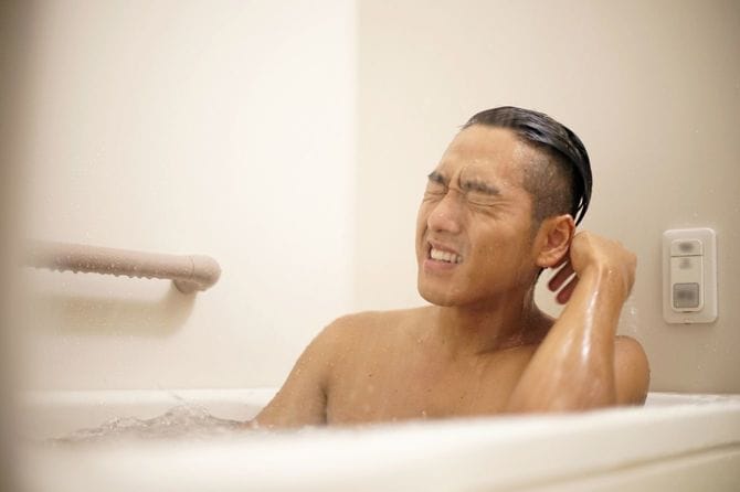 湯船に浸かりながら顔にシャワーを浴びる若い男