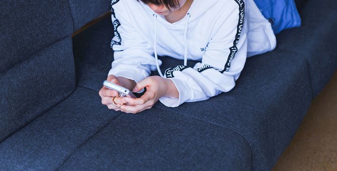 自宅のソファでスマートフォンを見ている日本人の女の子