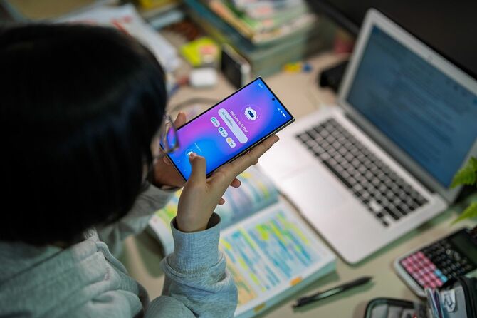 デスクで勉強しながらスマートフォンのAIチャットボットを使用する10代の少女