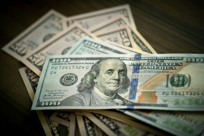 机に置かれた、数枚の50ドル紙幣と100ドル紙幣