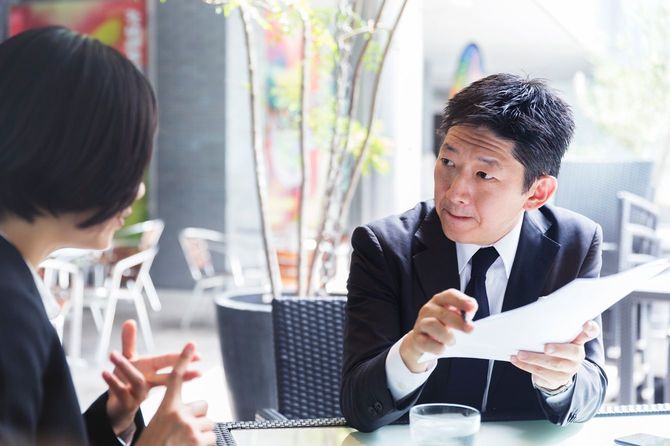 日本人経営者がクライアントの女性と業務契約の内容を詳細に話し合っている。