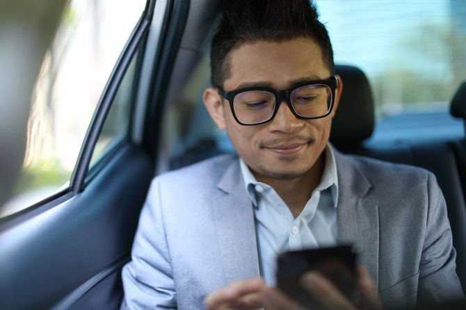 車の後部座席でメッセージを確認し、にやける男性