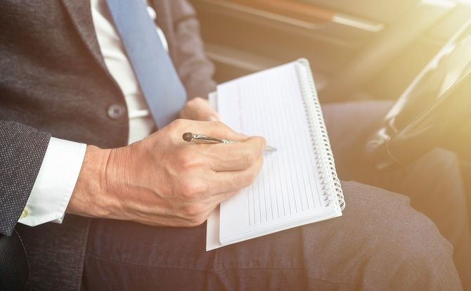 スーツを着て車に座っている間、メモを取るビジネスマンの手