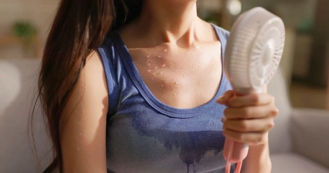 ハンディファンを使用しているタンクトップ姿の女性