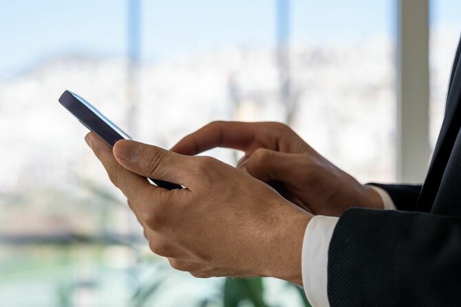 シティビューのモダンなオフィスでスマートフォンを使用するビジネスマン