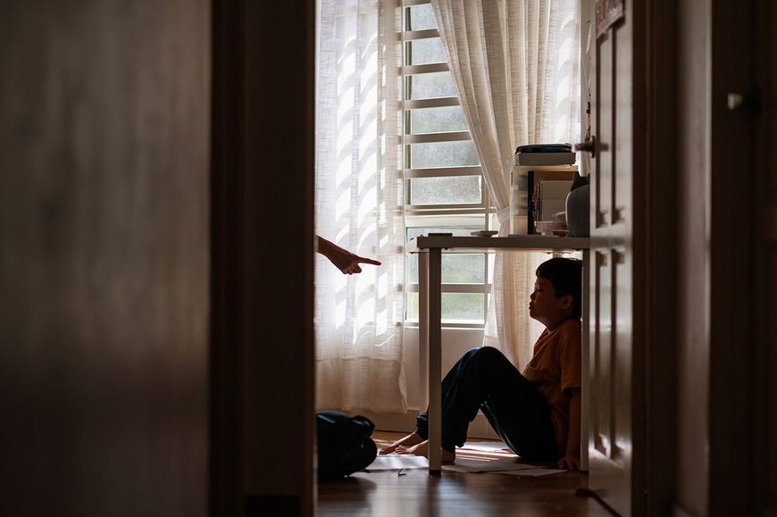 親に叱られてテーブルの下に隠れる子供