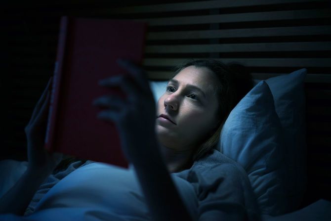 夜にベッドで本を読んでいる女性