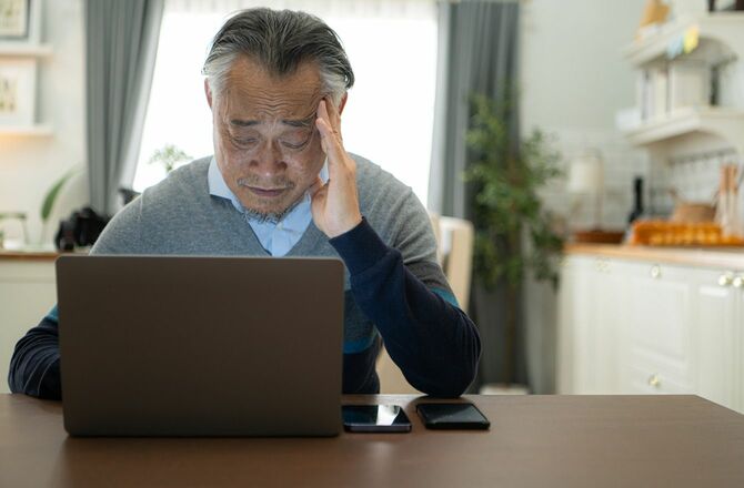 頭を悩ませながらラップトップに向かう高齢男性