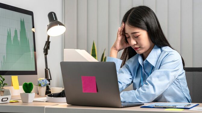 パソコンに向かって座り頭痛をこらえている女性