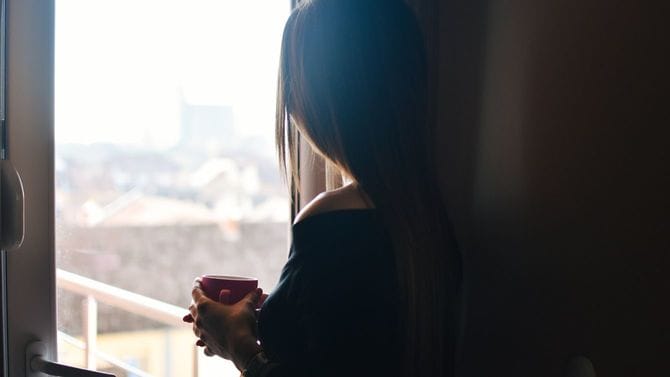 女性が一人、マグカップを手に窓の外を見つめている