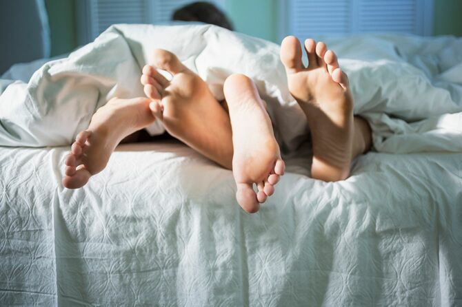 ベッドのうえにいる、布団から足元が見えているカップル