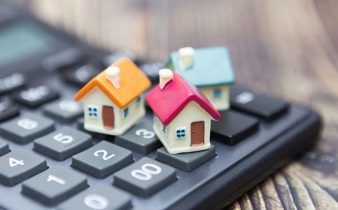 電卓の上に載っている3つのミニチュアハウス