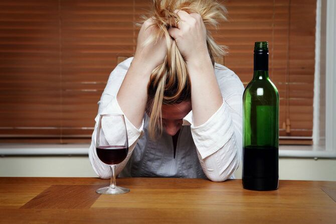 ワインを前に頭を抱えるアルコール依存症の女性