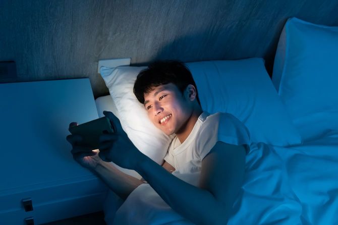 暗いベッドの上でスマートフォンを操作する若い男性