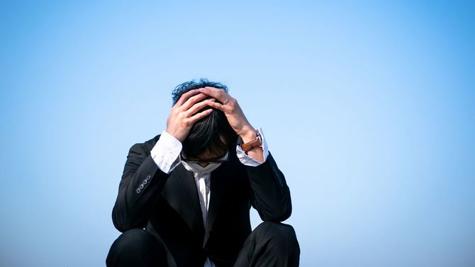 頭を抱えるマスクを着けた若い男性