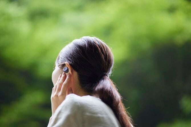 自然の中でイヤホンで何かを聴く女性