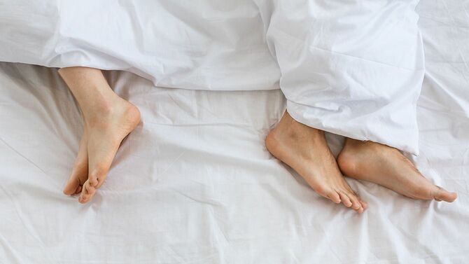 ベッドで背中を向けて寝る男女の足