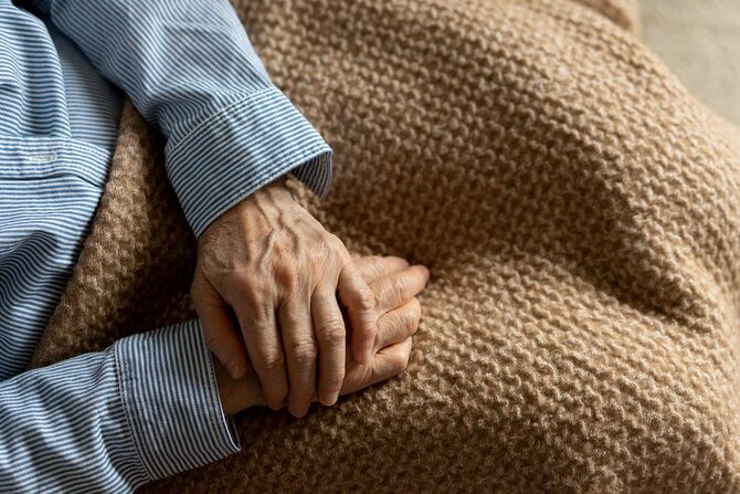 年配の女性が自宅のソファに座っています。 家のリビングルームで、ラップ毛布でソファに座っている静かなシーン。 高齢化社会。