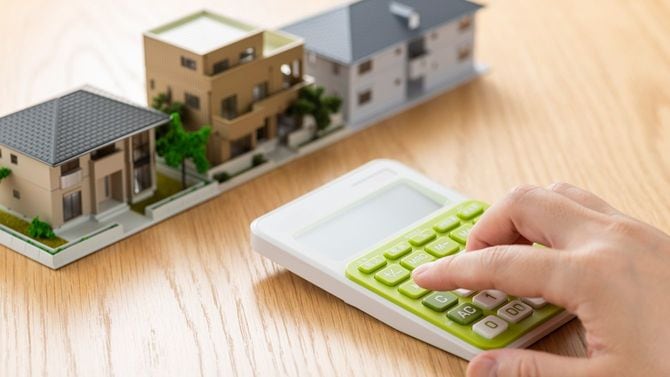 住宅模型の前で電卓をはじく男性