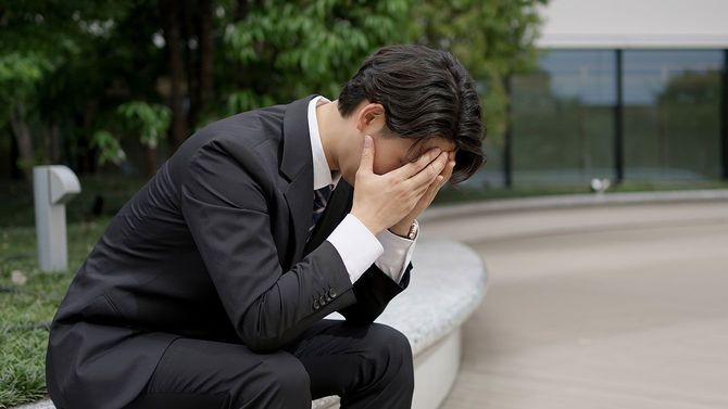 両手で顔を覆って落ち込んでいるビジネスマン