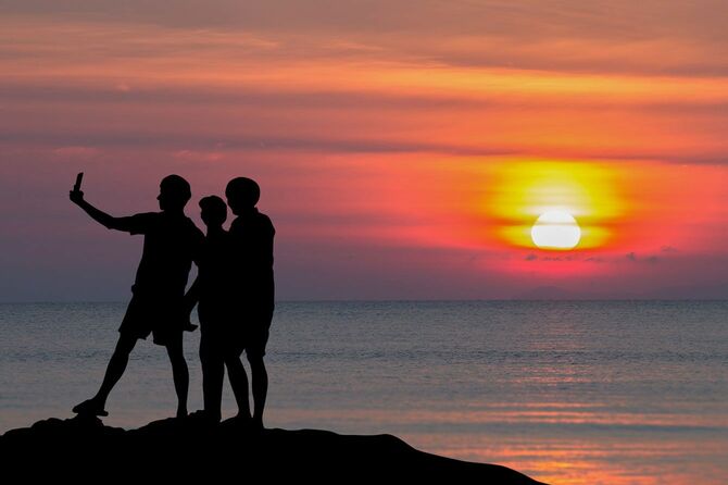 ビーチで夕日を背景に写真を撮る人たち