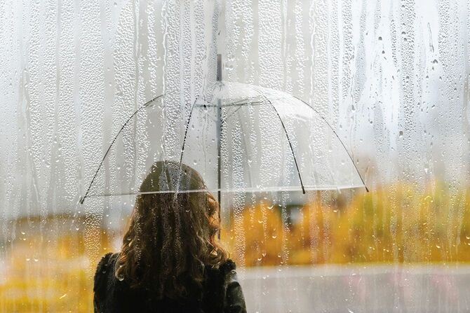 雨の中、傘を差してたたずむ女性の後ろ姿