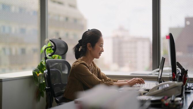 角部屋のオフィスで笑顔でオンラインミーティングに出席している女性