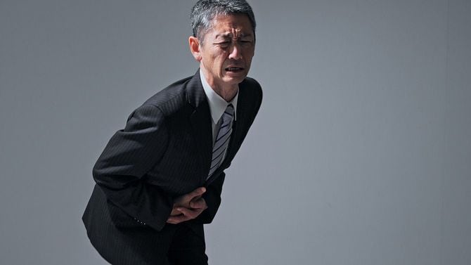 腹痛でお腹を両手で押さえている男性