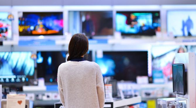 家電量販店のテレビ売り場で立ち尽くす女性