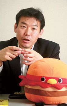 長らく店舗開発・調査畑を歩み、08年3月、マーケティング部シニアリーダーに就任した齊藤雅久氏。手前は、1972年東京・板橋生まれという設定のマスコットキャラクター「モッさん」。