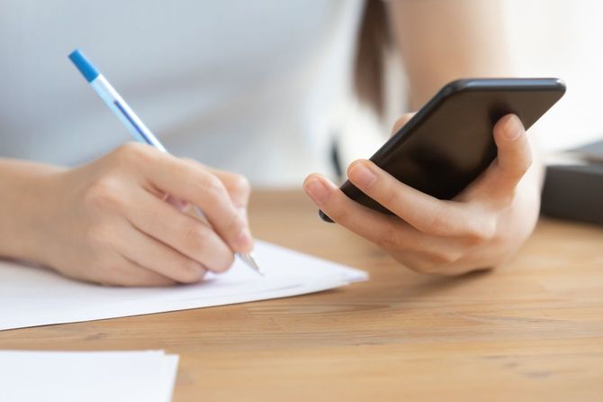 左手にスマホを持ち、右手でノートをとっている人の手元