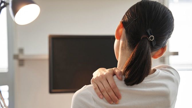 自宅勤務中、肩の痛みを覚え手でさする日本人女性